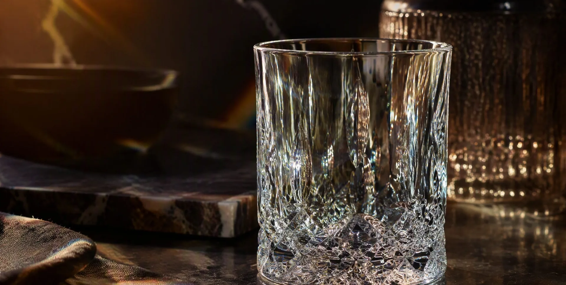 Artisan holding a lead-free crystal glass up to the light, fine luminous halos refracting through the walls