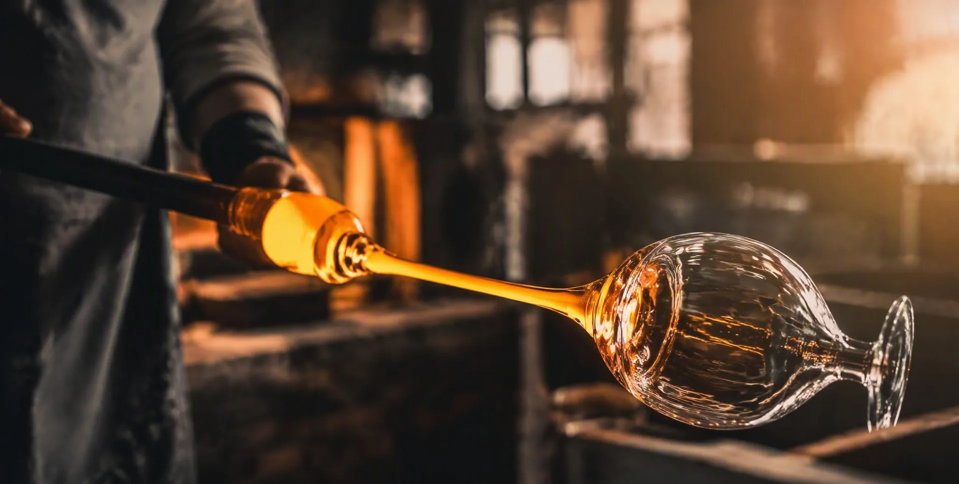 Glass artisan holding a wine glass by the stem, glow of the furnace reflected